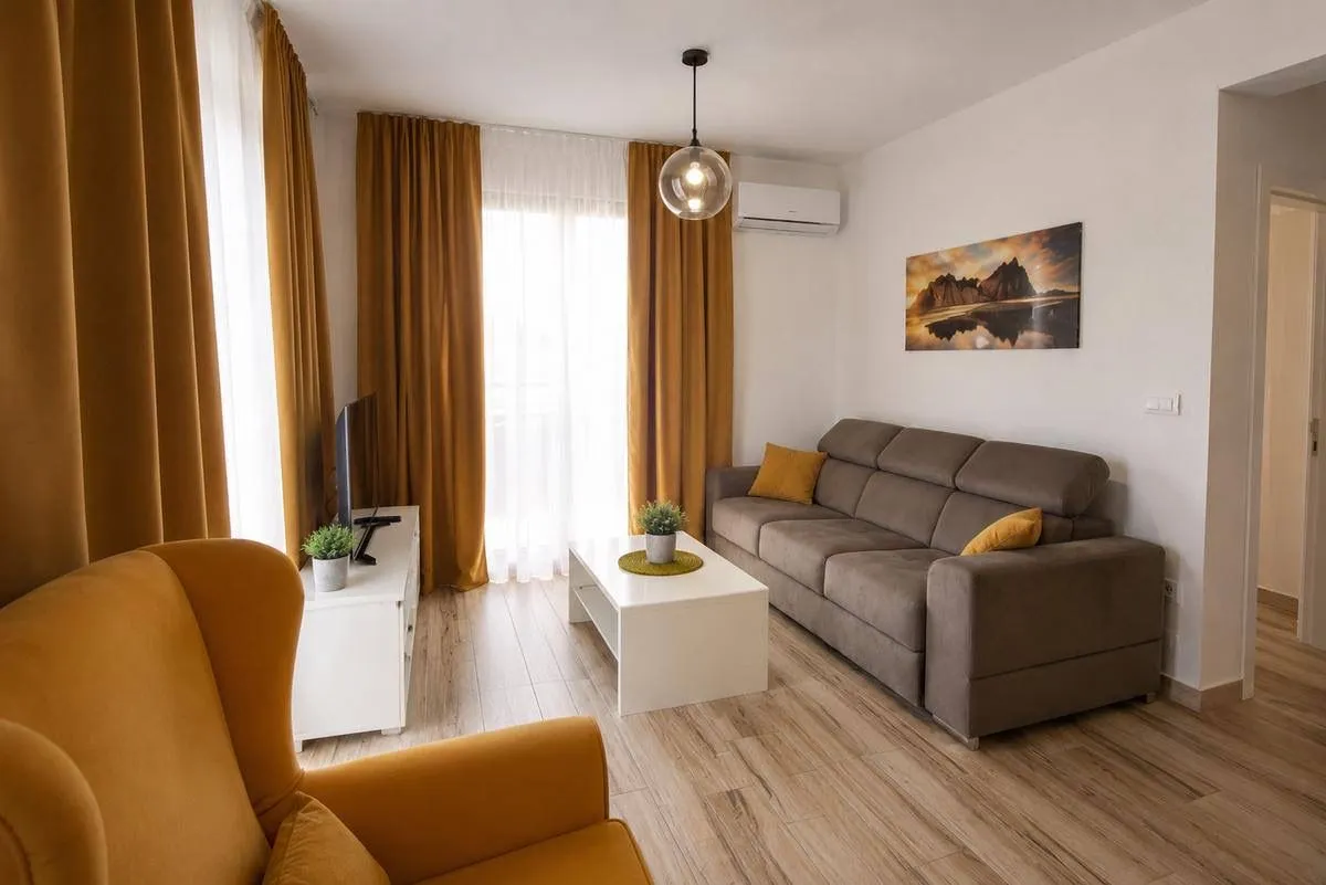 Bright living room with a sofa, armchair and large windows with yellow curtains.