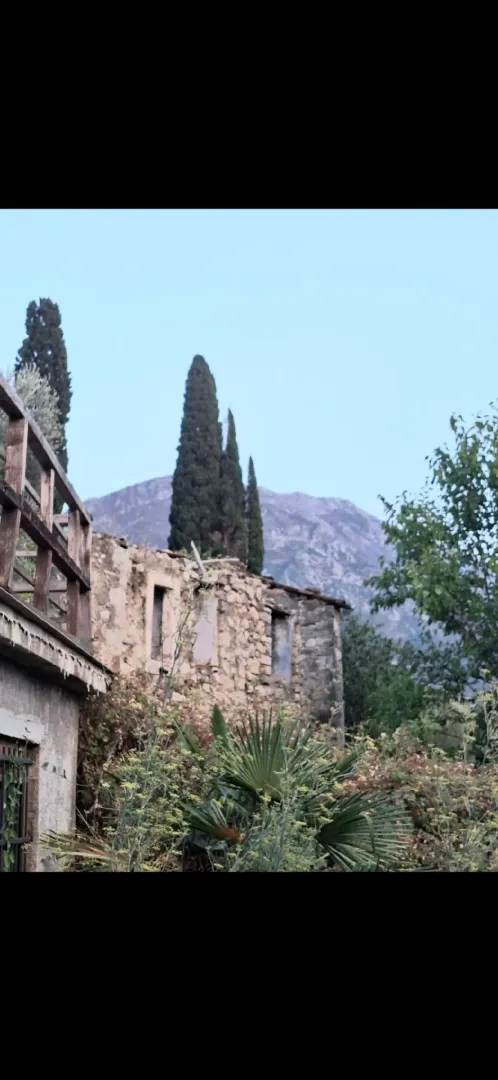 Pogled na staru kamenu kuću i dvori nijeme okružene zelenilom i planinama.