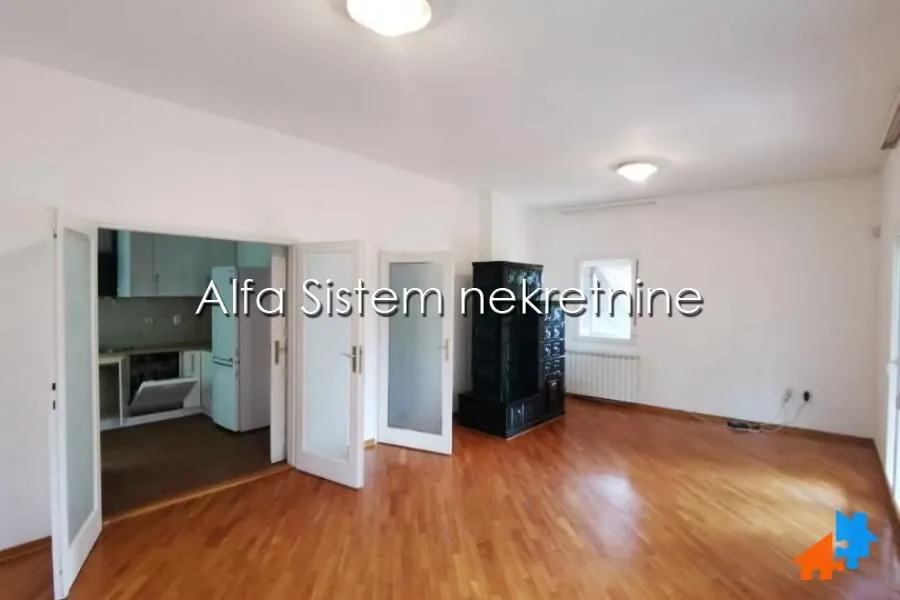 Spacious living room with hardwood floors and a solid fuel stove, looking into the kitchen.