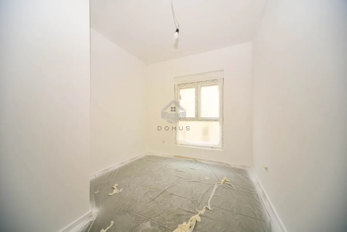 Empty unfinished room with white walls and a window covered in plastic sheeting.