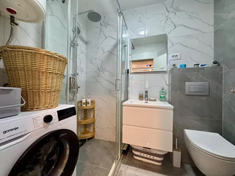 Modern bathroom with a shower cabin, sink, washing machine, and toilet. - image 6