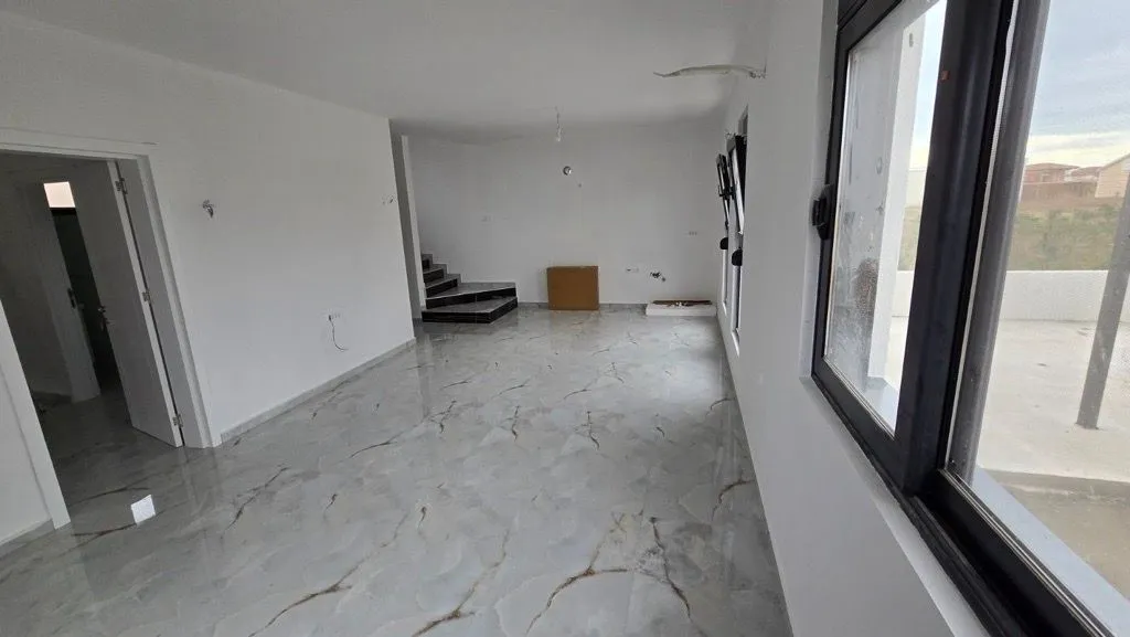 Prazna dnevna soba sa mermernim pločicama na podu i stepeništem u pozadini.