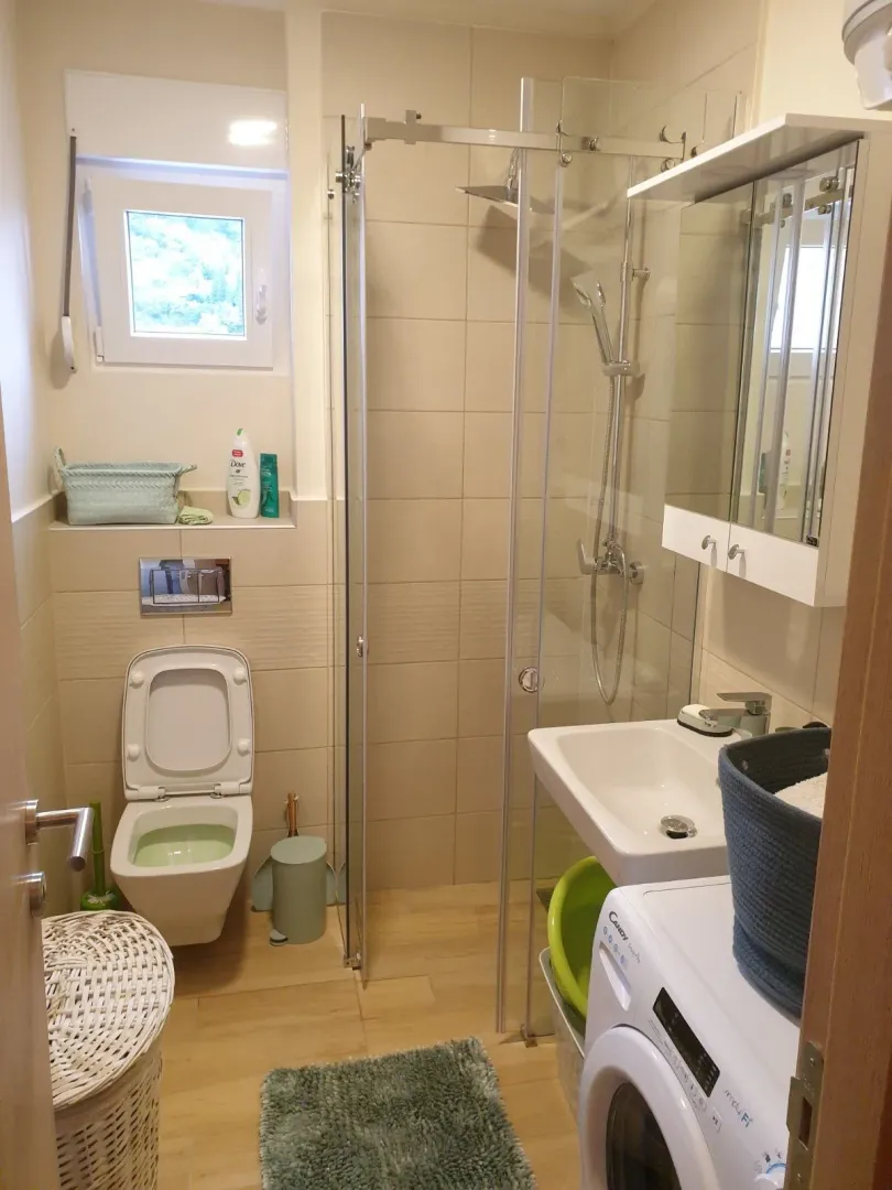 Manje kupatilo sa tuš kabinom, umivaonikom, toaletom i veš mašinom.