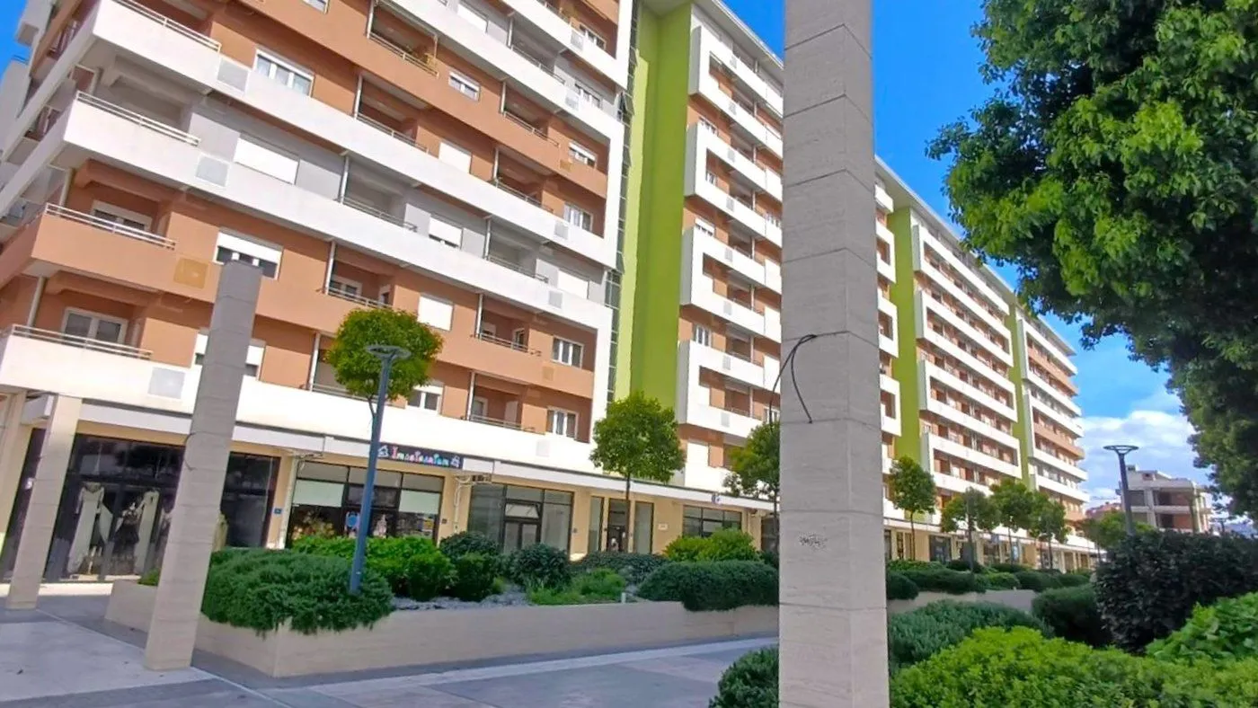Spoljašnji pogled na stambenu zgradu sa uređenim dvorištem i poslovnim prostorima u prizemlju.