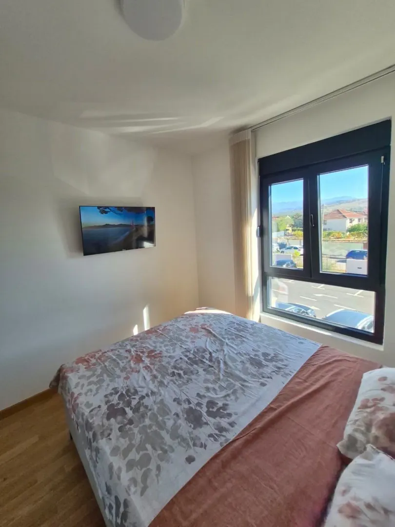 Namještena spavaća soba sa bračnim krevetom, televizorom na zidu i prozorom.