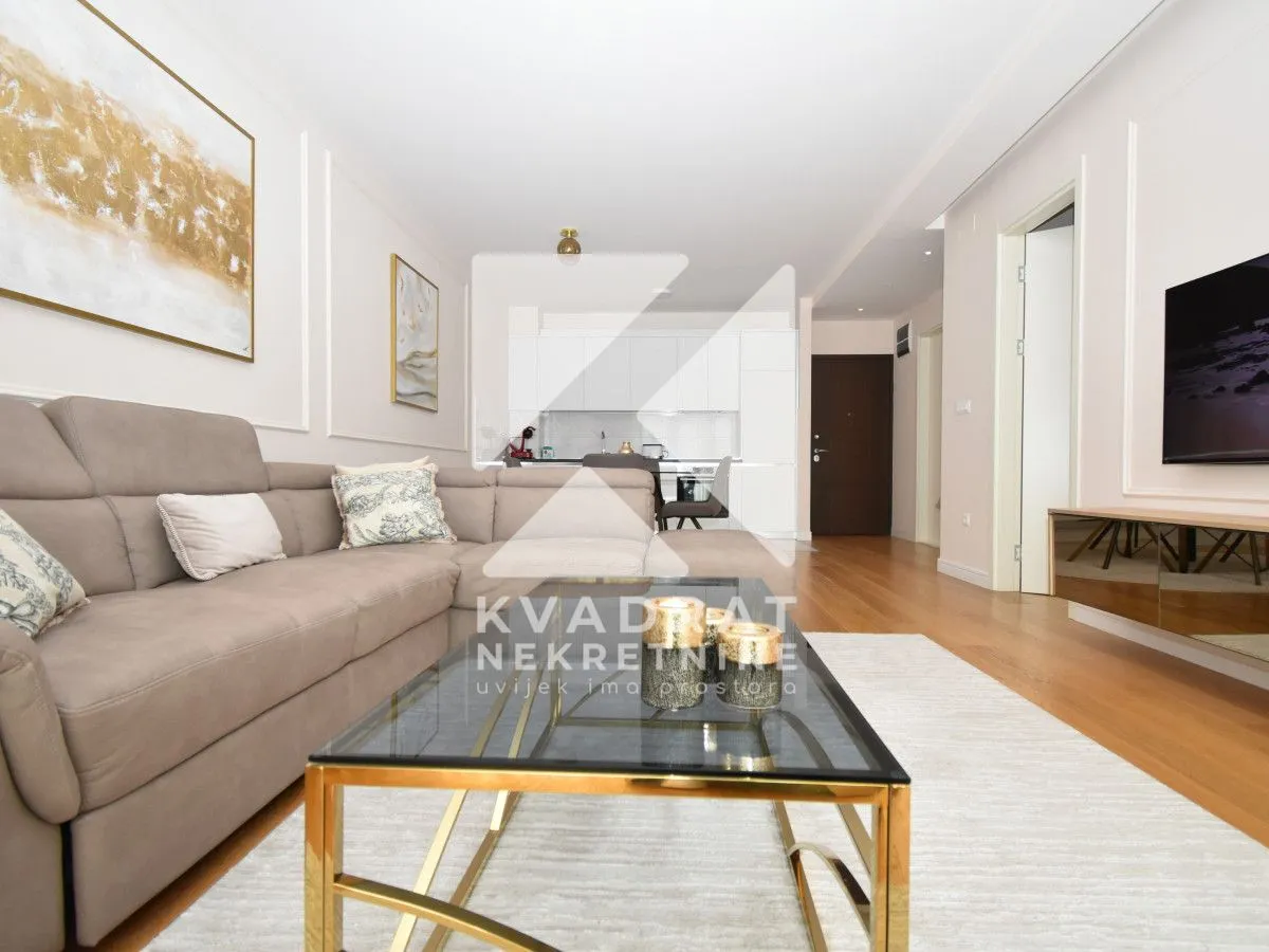 Living room with sofa, coffee table, and television, with a view of the kitchen.