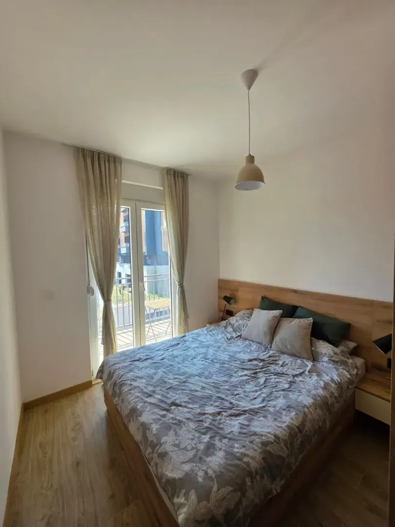 Svijetla spavaća soba sa bračnim krevetom i izlazom na balkon.