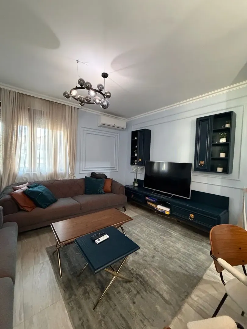 Dnevna soba sa garniturom, TV komodom i modernim lusterom.