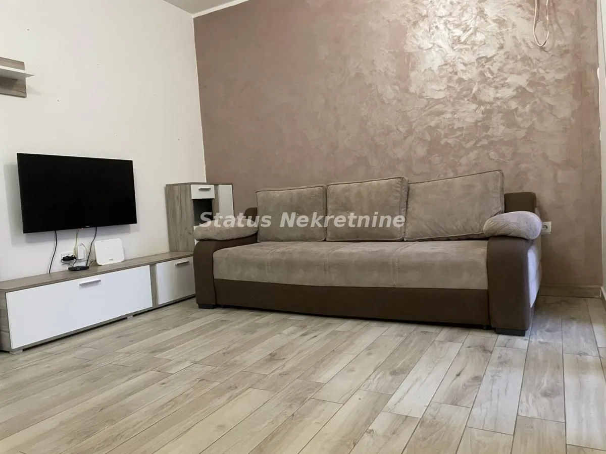 Dnevna soba sa ugaonom garniturom, televizorom i komodom.