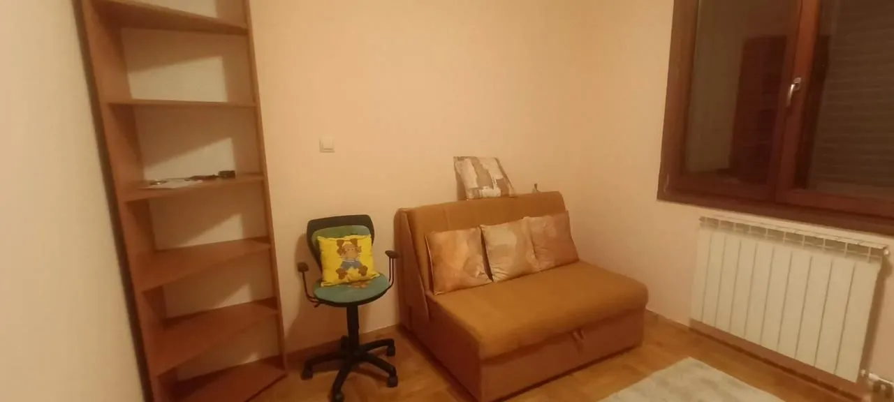Dnevna soba sa kaučem, radnom stolicom i drvenom policom.