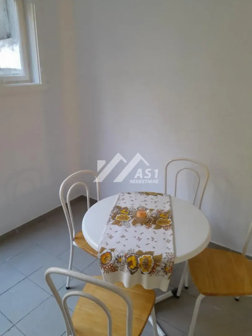 Manji trpezarijski sto sa četiri stolice u uglu prostorije.