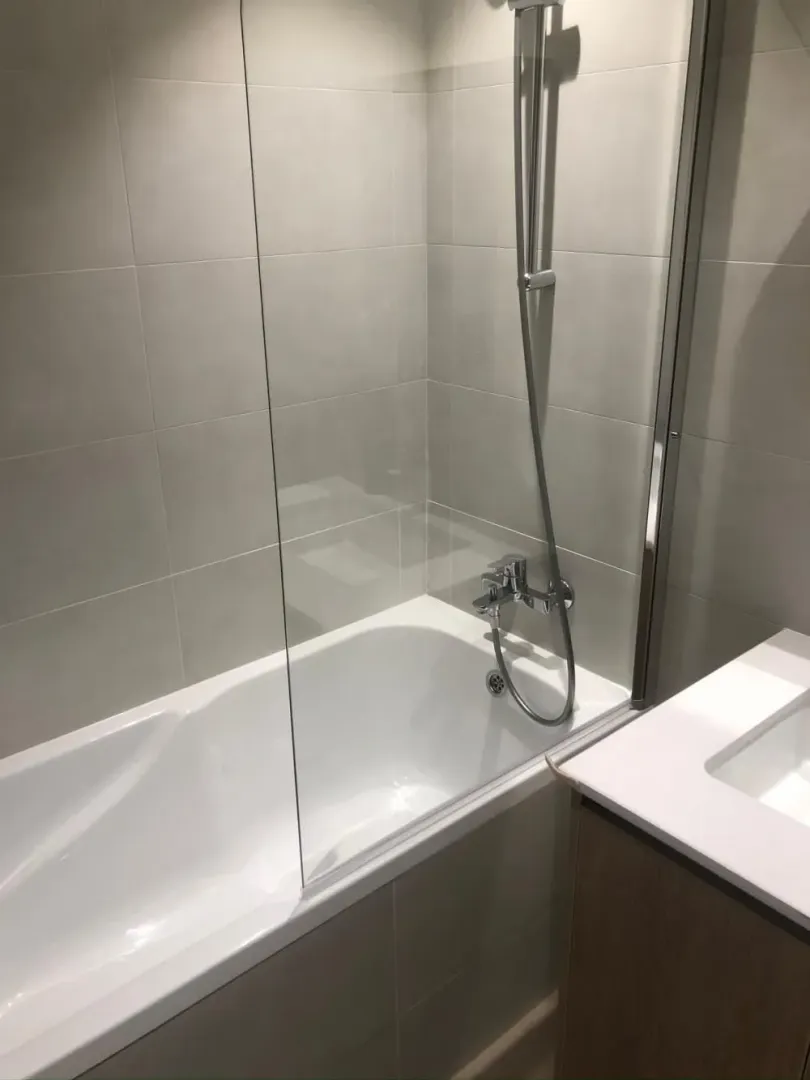 Modern bathroom with a bathtub, glass screen, and washbasin.
