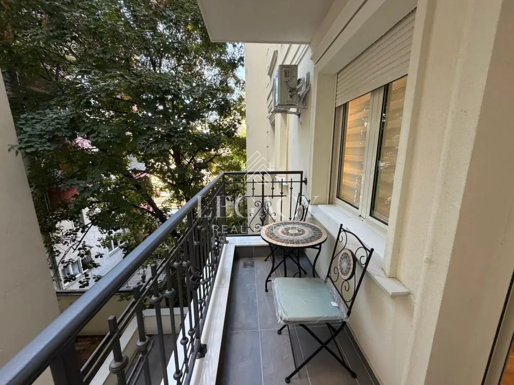 Small furnished balcony with metal railing and green view.