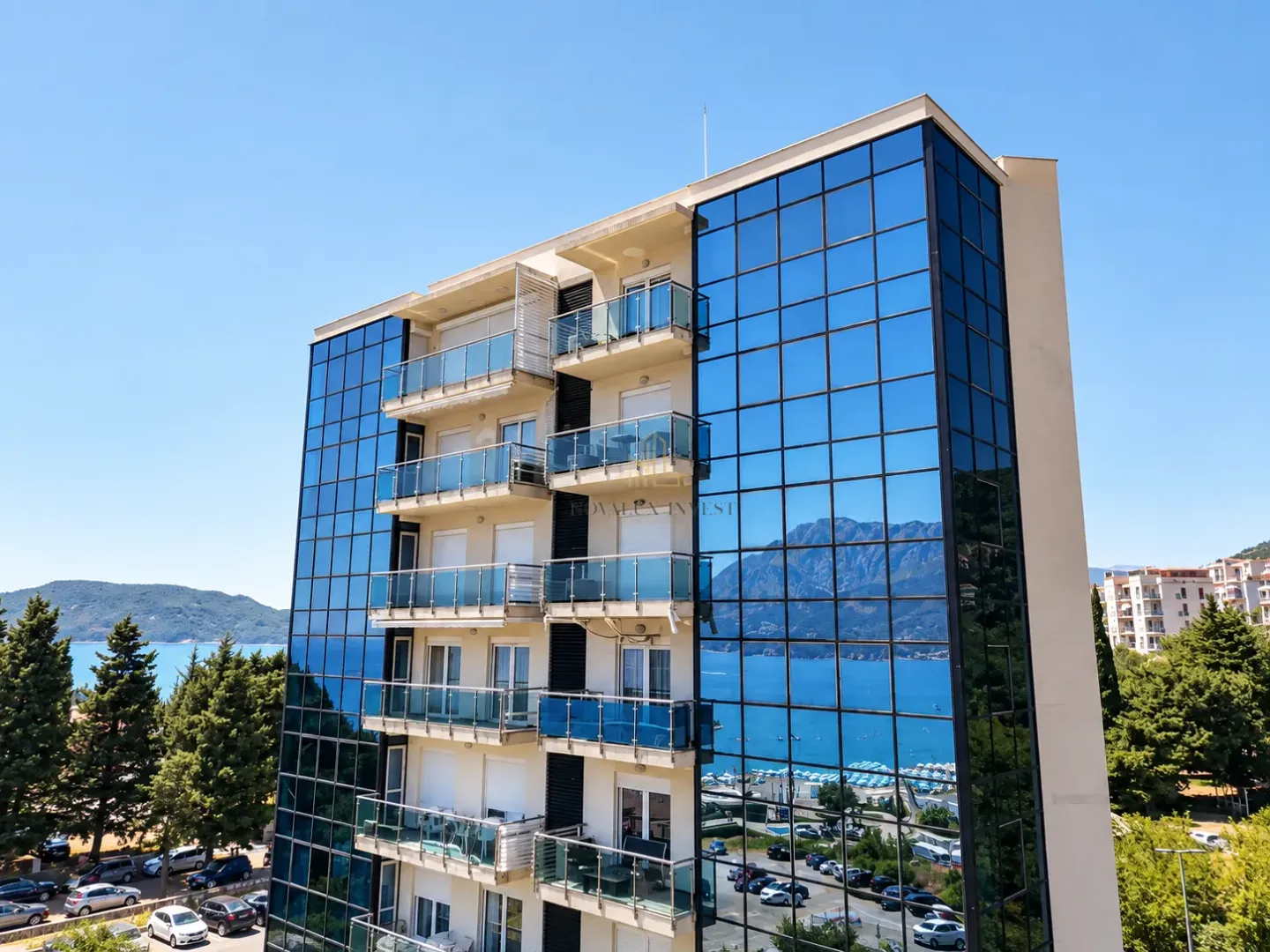 Pogled na modernu stambenu zgradu sa staklenom fasadom i balkonima u blizini mora.