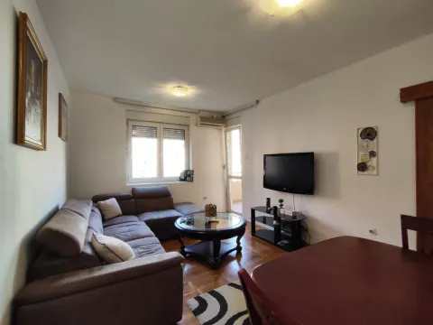Svijetla dnevna soba sa ugaonom garniturom i televizorom na zidu. - image 12