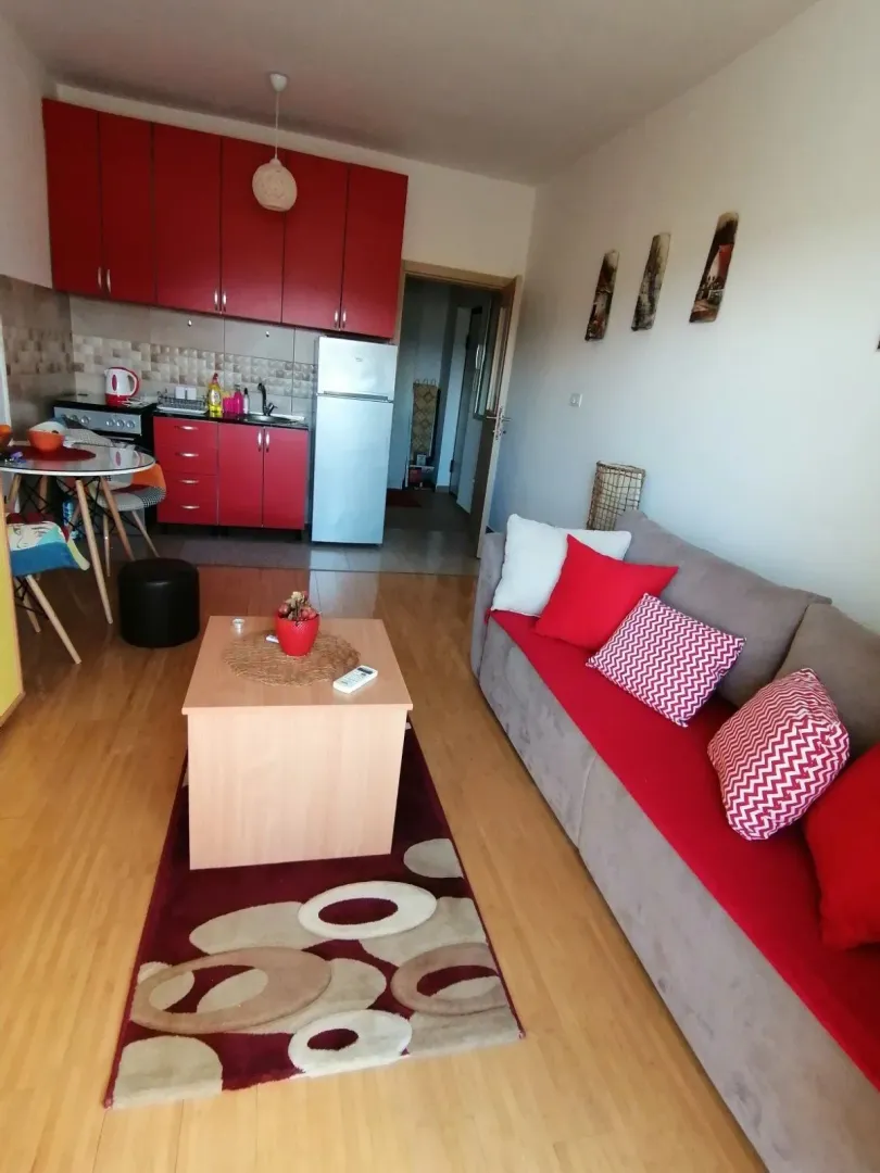 Living room with a red sofa and kitchen in the background.
