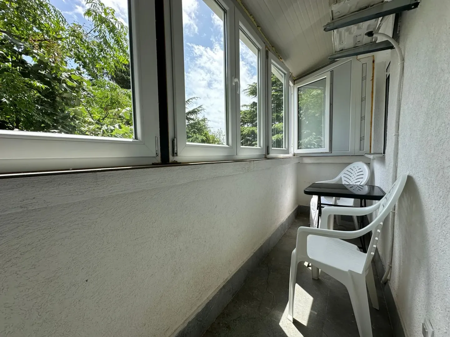 Zastakljeni balkon sa plastičnim stolom i stolicama.