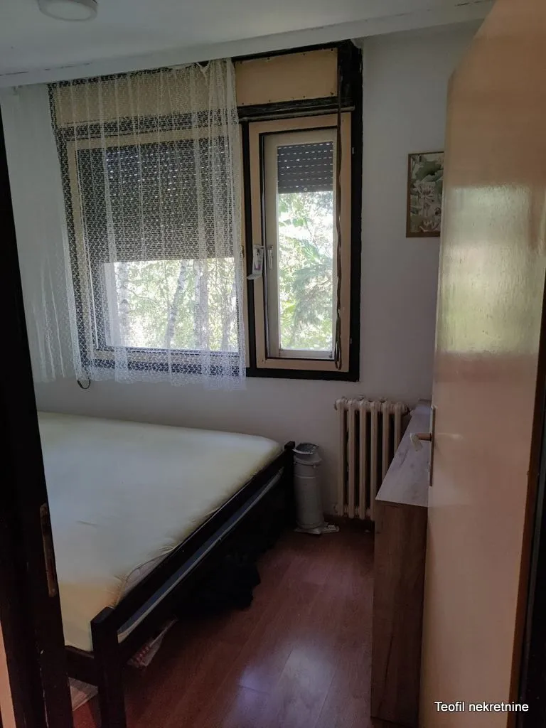 Manja spavaća soba sa krevetom i prozorom koji gleda na zelenilo.