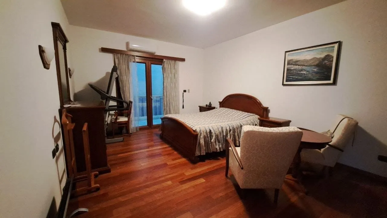 Spavaća soba sa bračnim krevetom, drvenim namještajem i izlazom na balkon.