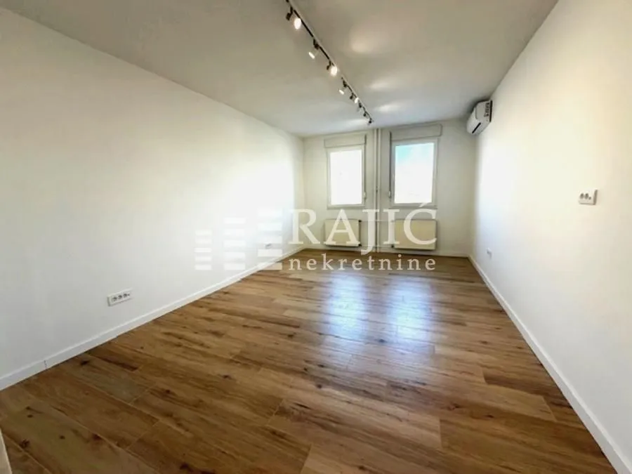 Empty room with wooden flooring and two windows.