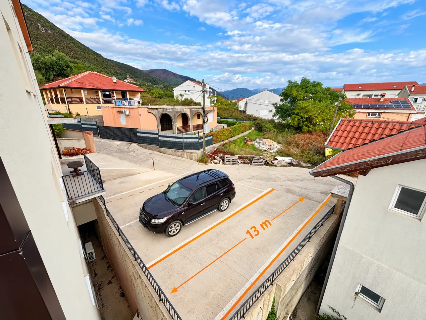 Pogled sa terase na parking prostor ispred zgrade sa okolnim kućama.