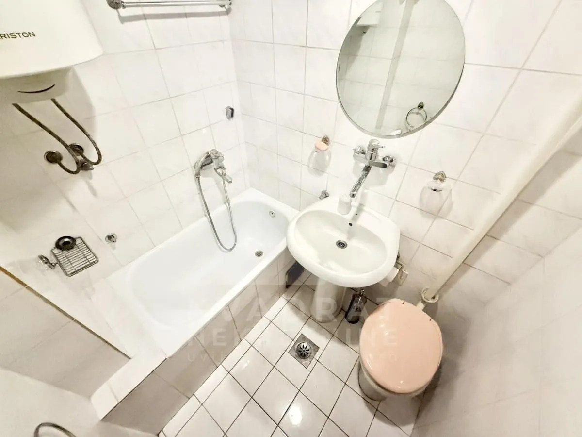 Manje kupatilo sa kadom, umivaonikom, toaletom i bijelim pločicama.