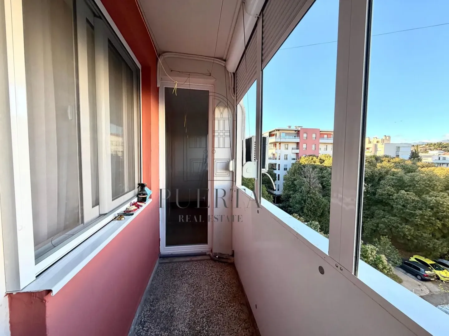 Enclosed balcony with a view of surrounding buildings and greenery.