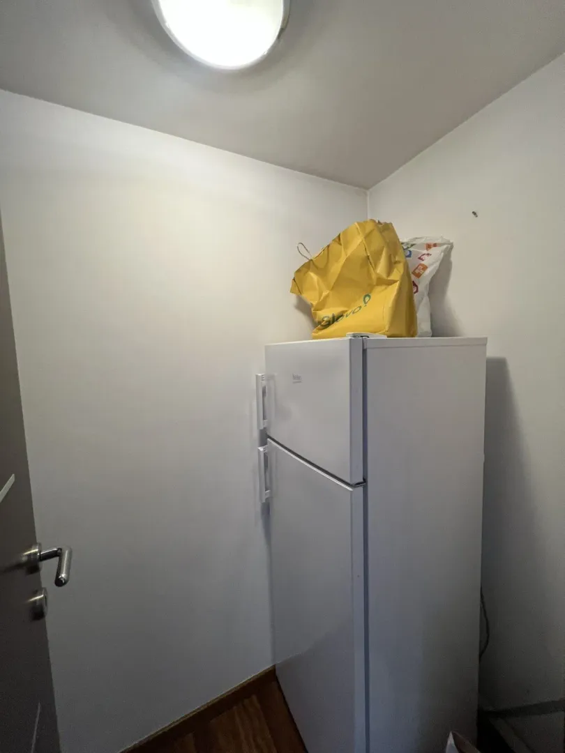 A white refrigerator placed in the corner of a room.