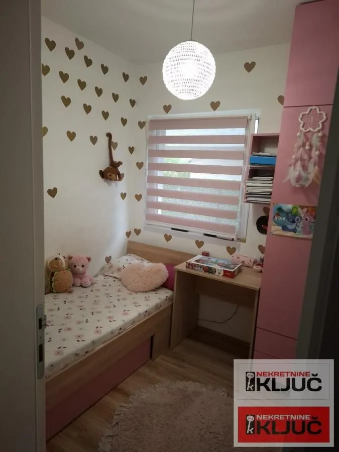 Dečja soba sa krevetom, radnim stolom i roze ormarom.