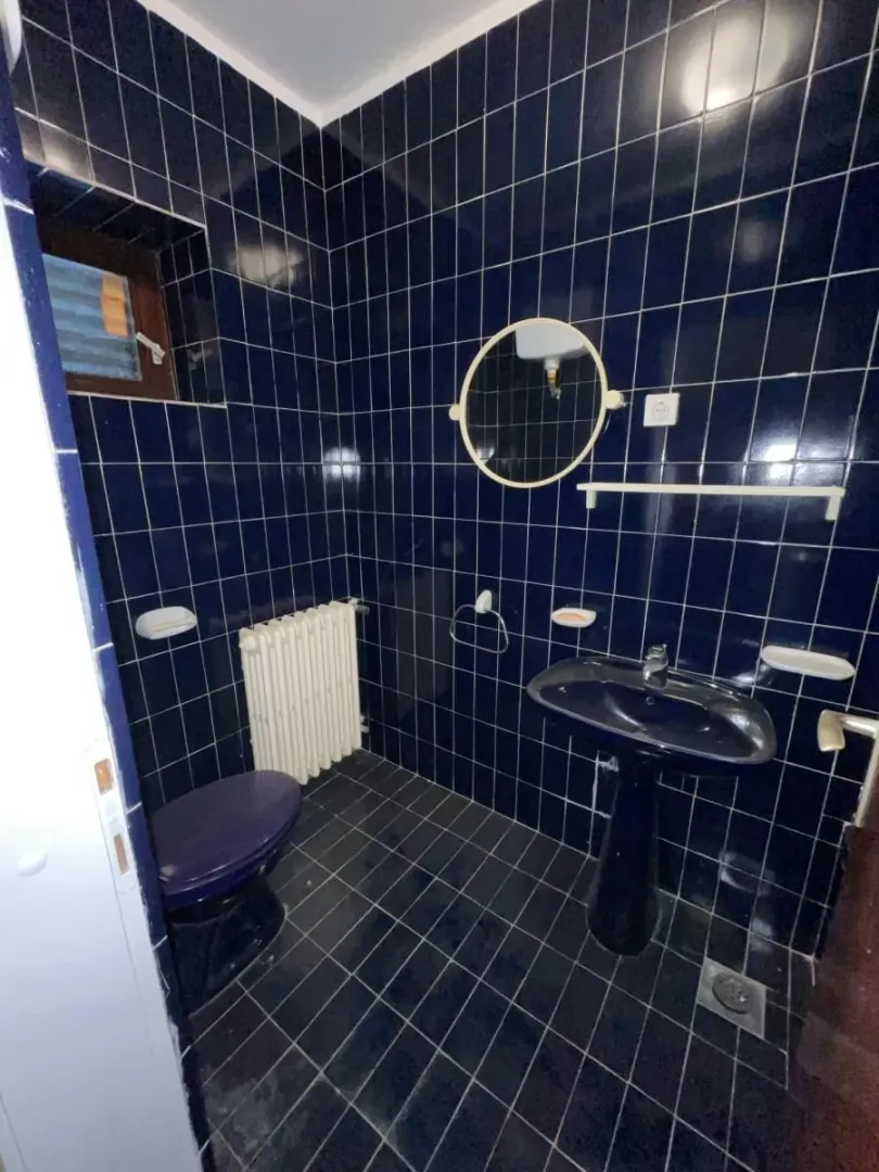 Kupatilo obloženo tamnoplavim pločicama sa umivaonikom, WC šoljom i ogledalom.