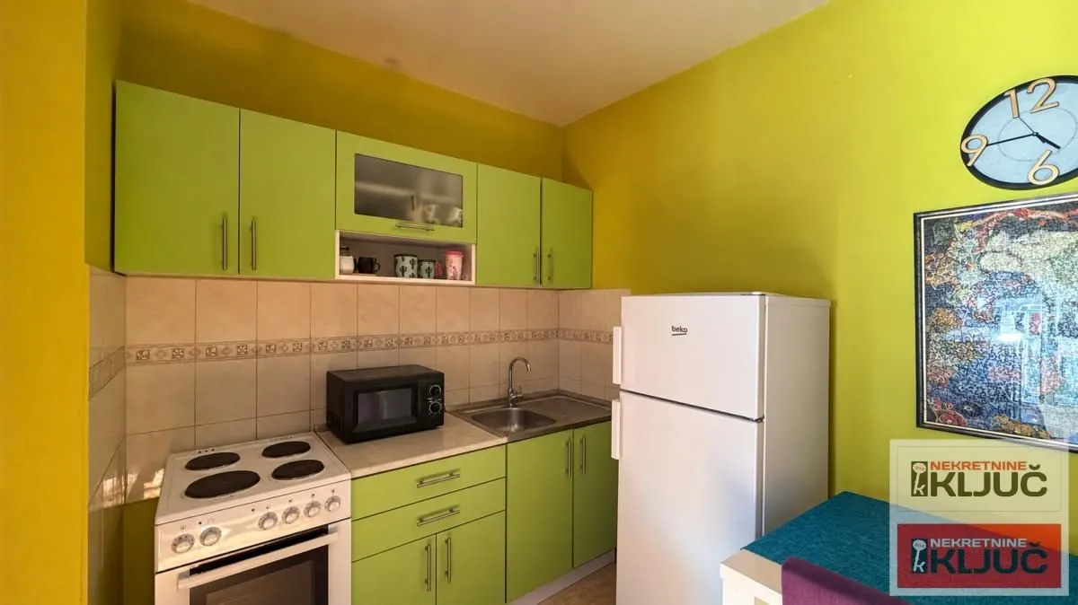 Manja kuhinja sa zelenim elementima i belim kućnim aparatima.