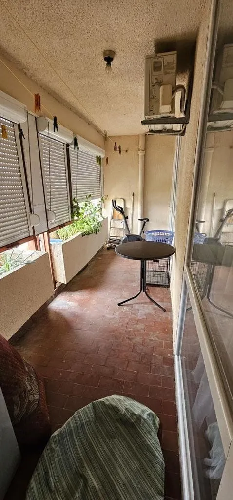 Zastakljeni balkon sa stolom, klima uređajem i prostorom za odlaganje.