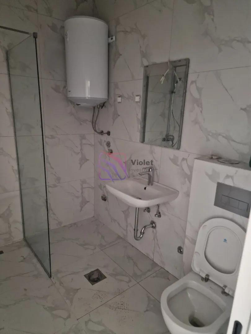 Manje kupatilo sa tuš kabinom, umivaonikom, wc šoljom i bojlerom obloženo mermernim pločicama.