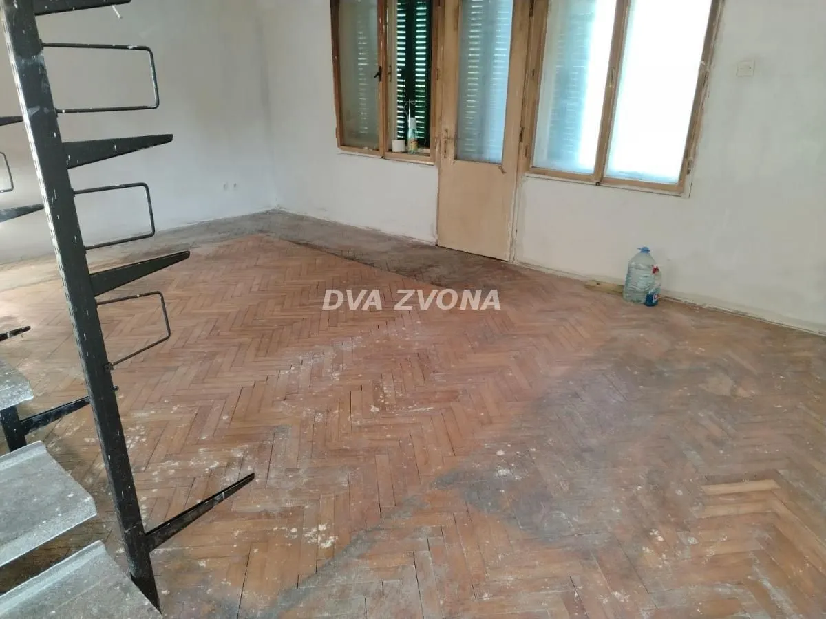 Prazna prostorija sa drvenim parketom i stepeništem.