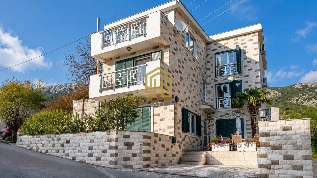 A modern three-story house with a stone facade and a fenced yard.