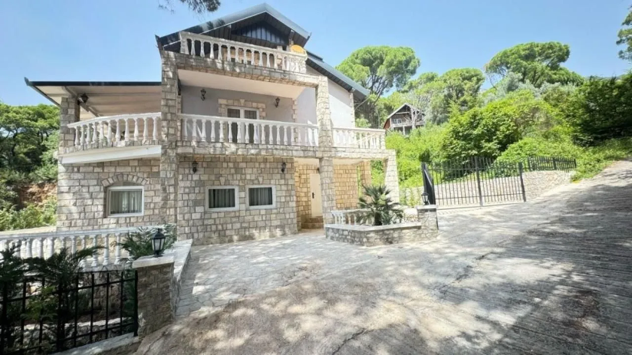 Pogled na eksterijer dvospratne kamene kuće sa terasama i dvorištem.