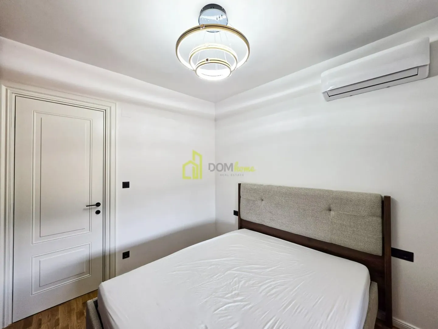 Bright bedroom with a double bed, air conditioning, and a white door.