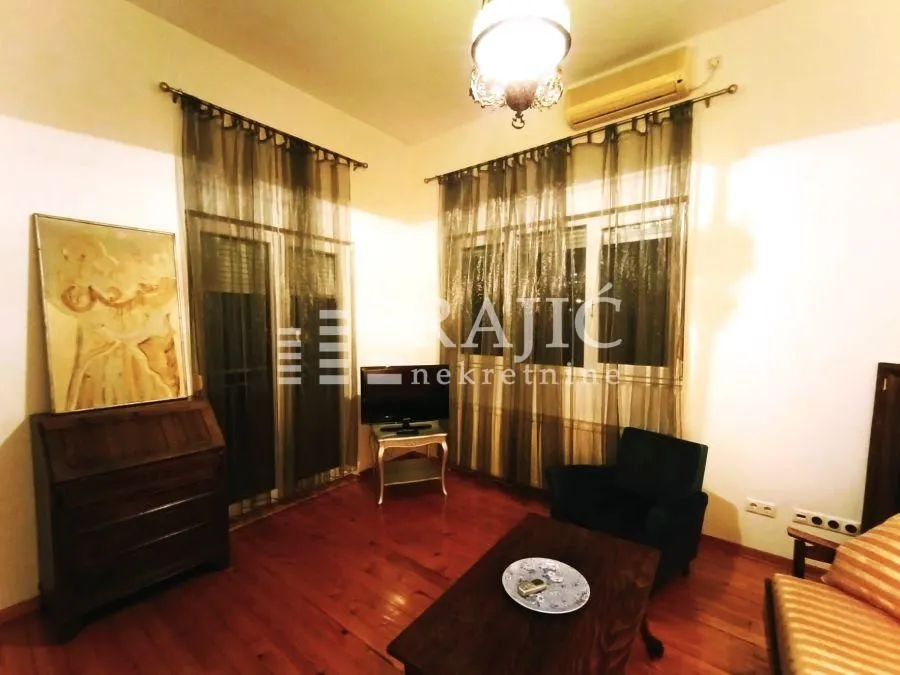 Living room with wooden flooring, furniture, and windows with dark curtains.