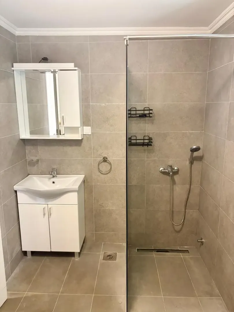 Modernly equipped bathroom with a shower cabin and a vanity with a mirror.