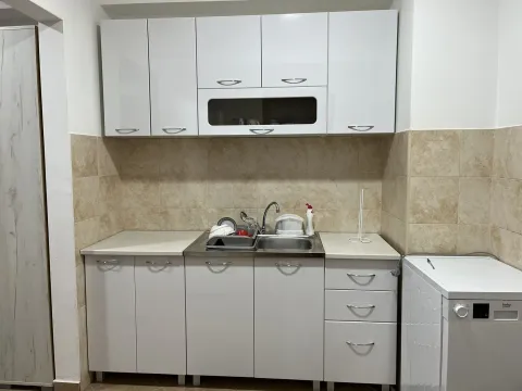 A simple kitchen with white cabinets, a sink, and a washing machine. - image 8