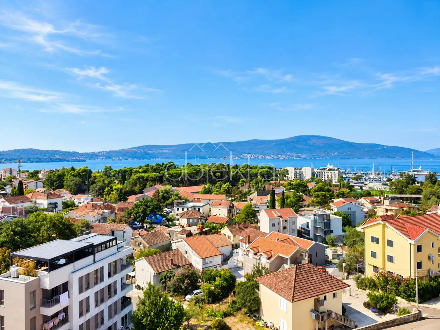 Pogled sa nekretnine na grad, okolno zelenilo i more u daljini.