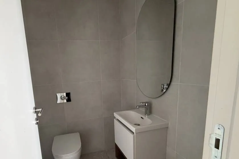Moderno opremljeno kupatilo sa sivim pločicama, umivaonikom i ugradnom wc šoljom.