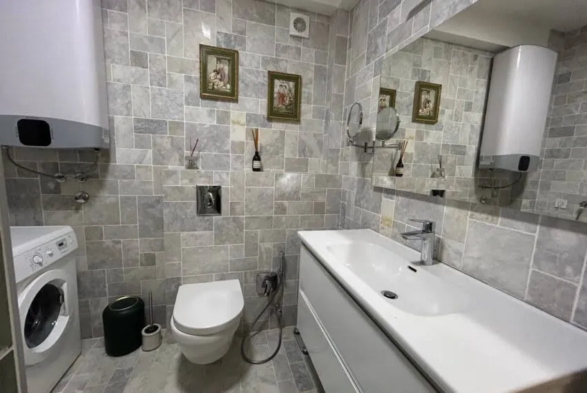 Potpuno opremljeno kupatilo sa svijetlim pločicama, umivaonikom, WC šoljom i veš mašinom.