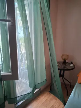 View of a window with green curtains and a small table with a lamp in the bedroom. - image 11