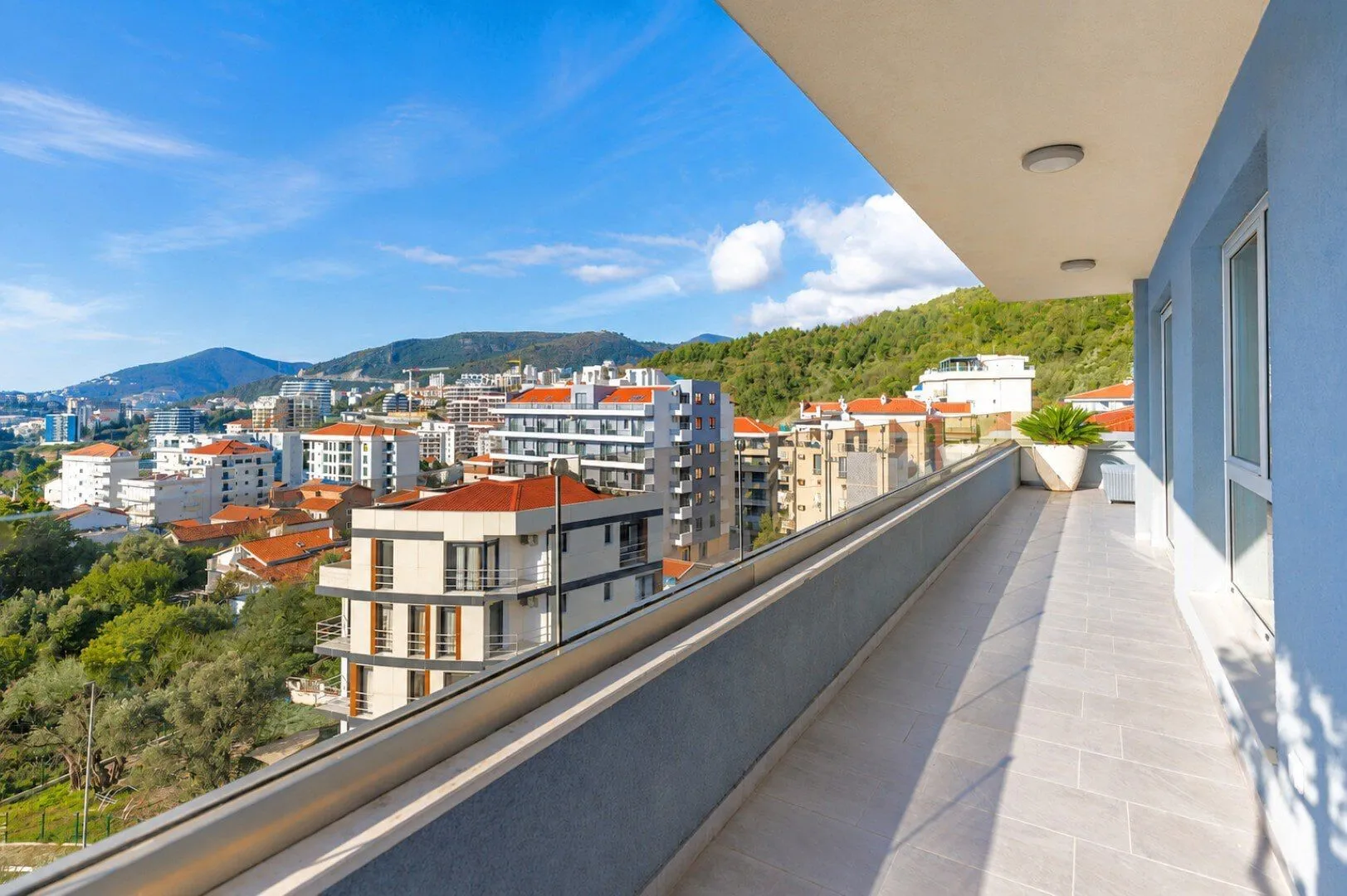 Prostrani popločani balkon sa staklenom ogradom i pogledom na grad i brda.