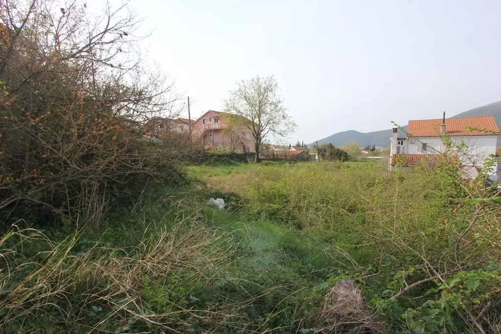 Travnati plac okružen kućama i zelenilom podno brda.