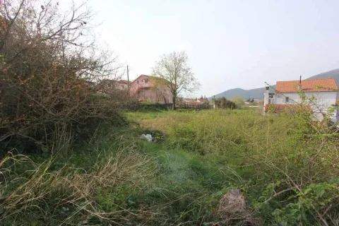 Travnati plac okružen kućama i zelenilom podno brda. - image 4