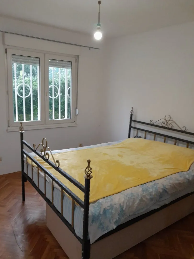 Spavaća soba sa metalnim krevetom i žutim prekrivačem pored prozora.