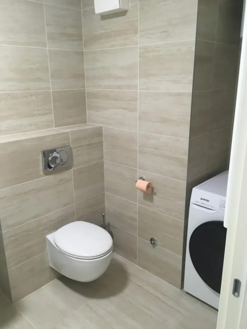 Bathroom tiled in beige with a wall-mounted toilet and washing machine.