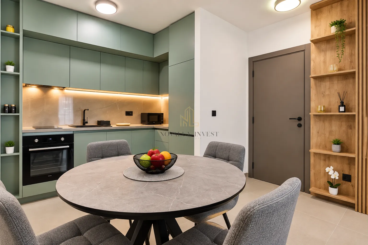 Modern kitchen with green cabinets, dining table and grey chairs.